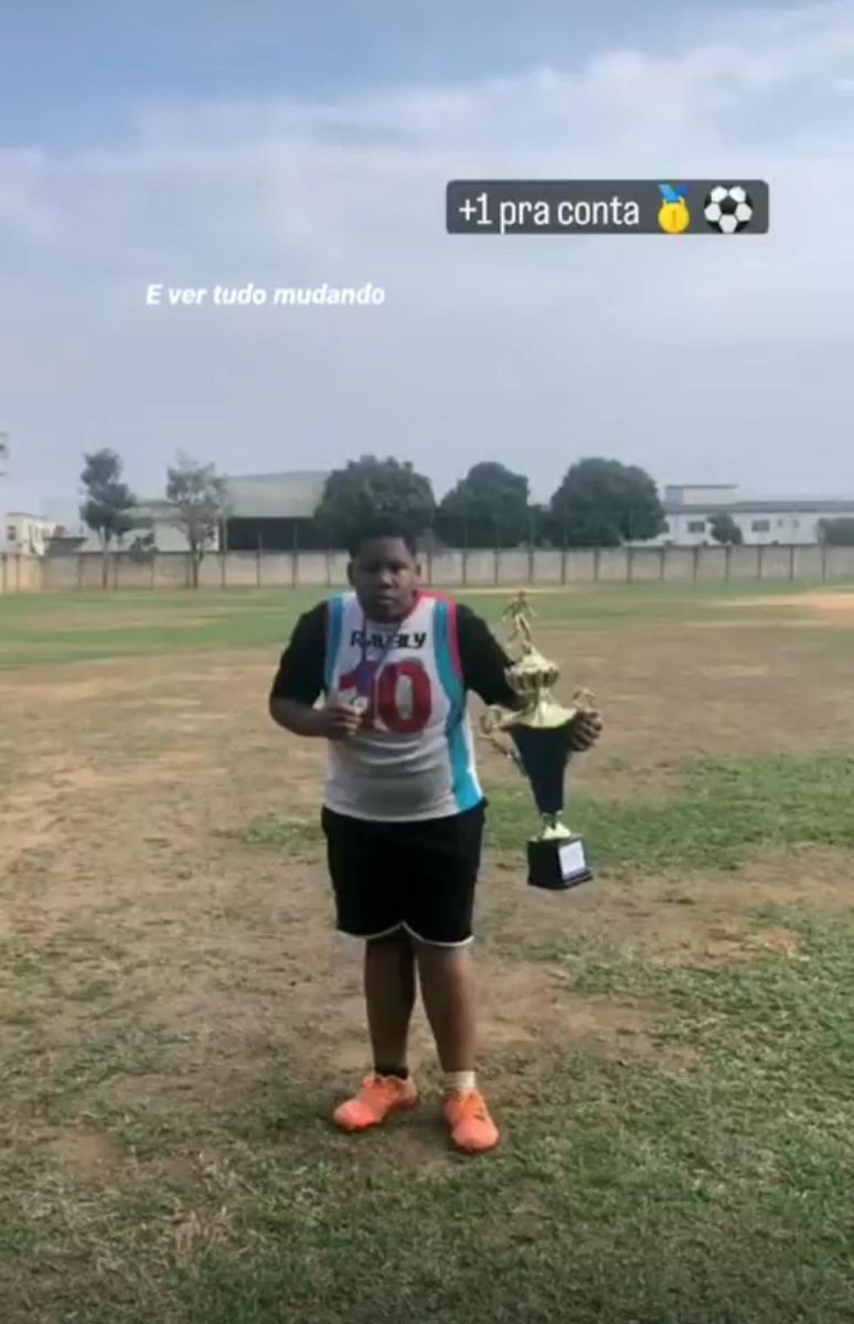 Aluno antes do acompanhamento, segurando troféu em campo de futebol